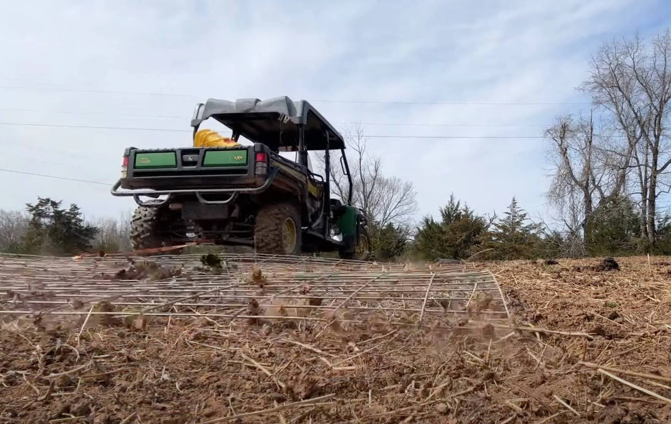 John Deere Gator pulling cattle panels across a pasture to spread manure—a DIY solution replacing a commercial pasture drag.